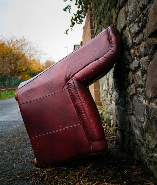 An old, worn-out sofa with a floral patterned fabric on the backrest and armrest, and a dark brown velvet material on the seat cushion, is situated outdoors on a paved surface. The sofa shows signs of